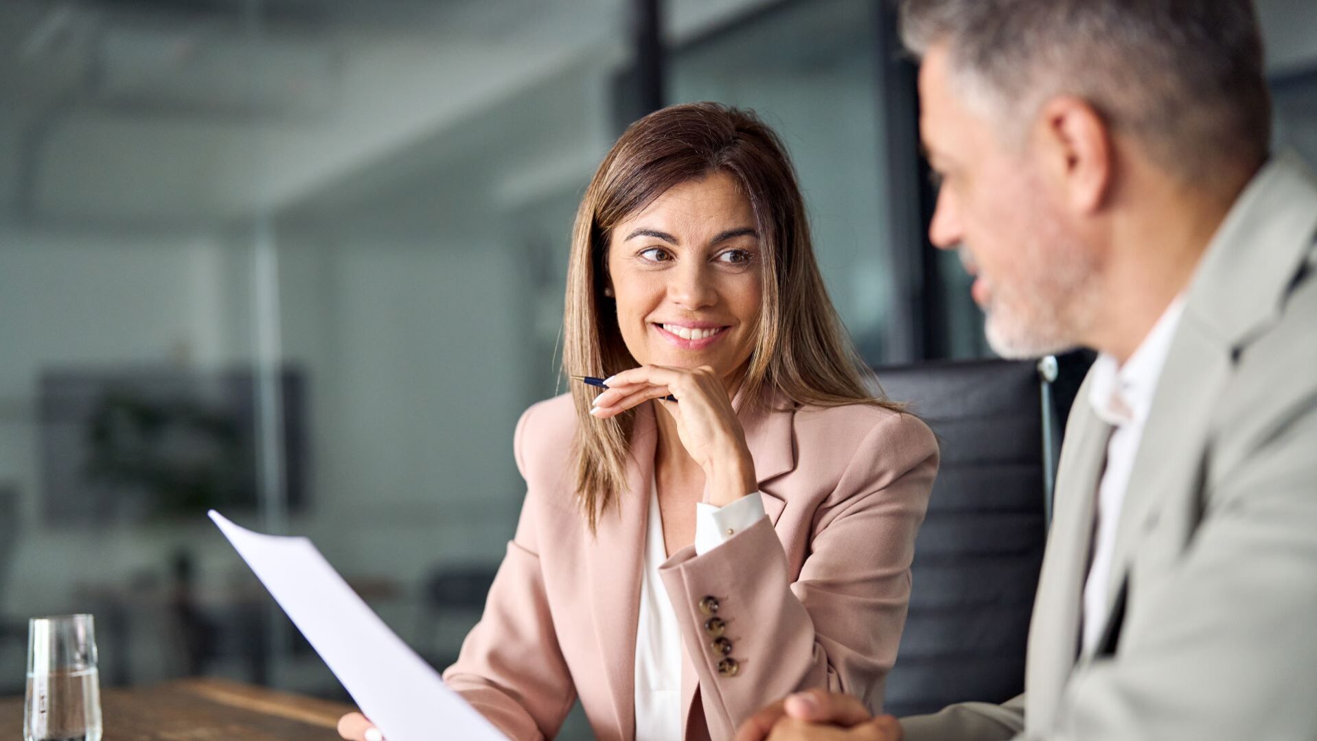 Two business executives discussing financial legal papers in office at meeting. Smiling female lawyer adviser consulting mid aged client at meeting. Mature colleagues doing project paperwork overview.